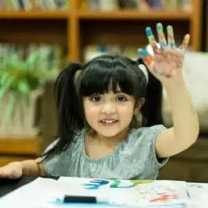 A cute girl is decorating a card with her hand prints- Mother’s Day activities for kids