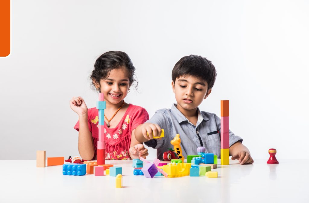 cute-little-indian-asian-kids-playing-with-colourful-plastic-toys-blocks-while-sitting-table-isolated-